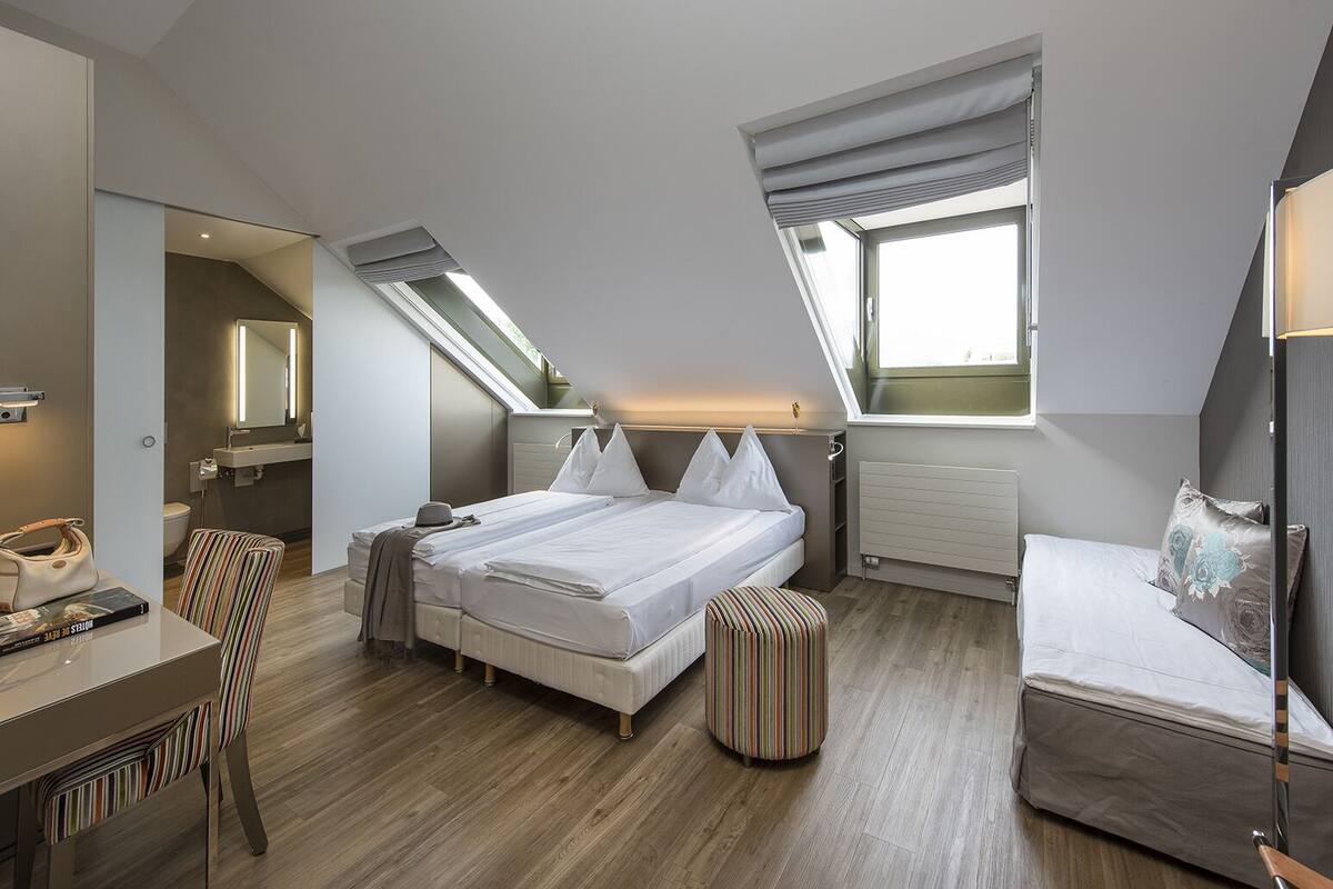 A modern bedroom with a large bed, a desk, and a small seating area.