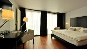 A hotel room with a bed, a desk, a chair, a lamp, and a window with curtains.