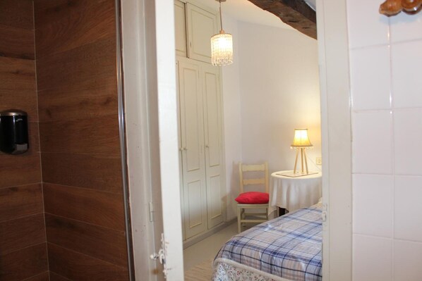 Une chambre avec une armoire en bois, un lit recouvert d’une couverture à carreaux, une petite table avec une lampe et une chaise.