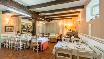 A dining area with multiple tables and chairs, wooden beams on the ceiling, and a wine rack in the background.
