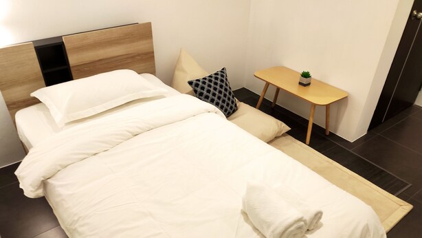 Una cama bien hecha con sábanas blancas, cabecera de madera y una mesita de noche con una planta.