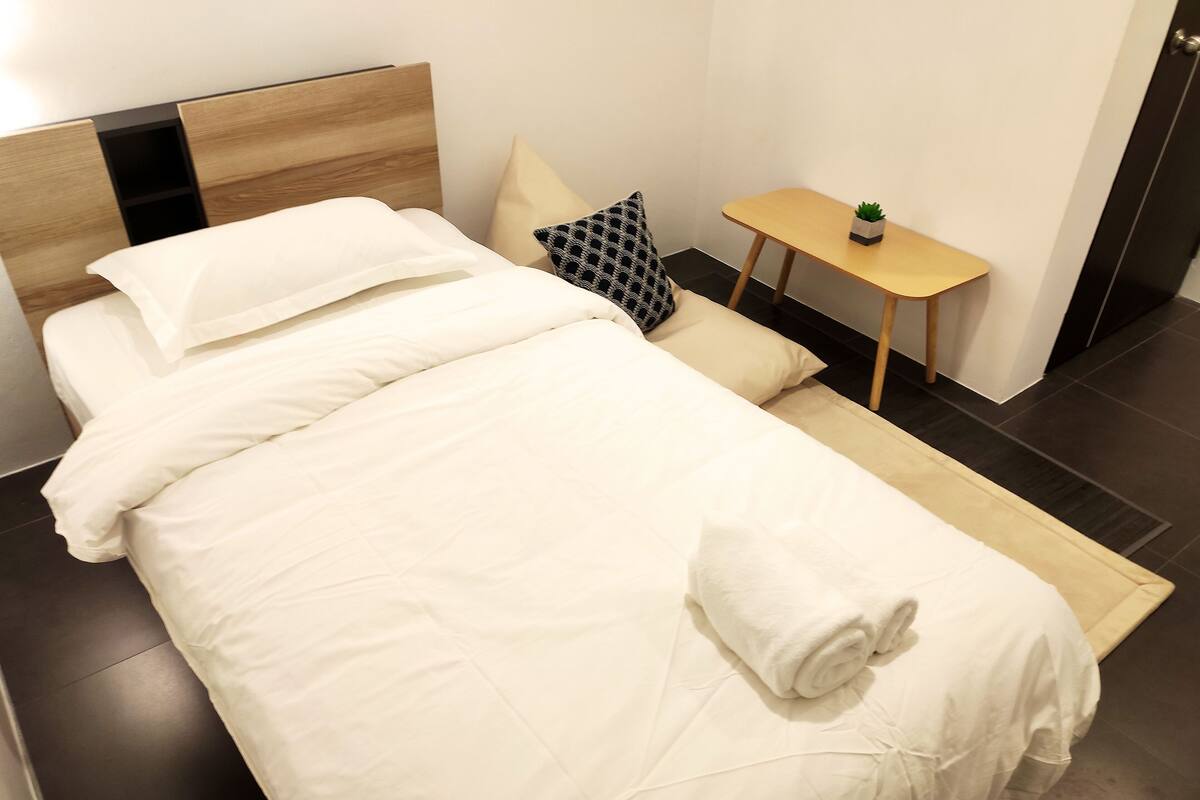 A neatly made bed with white linens, a wooden headboard, and a small bedside table with a plant.