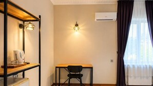 A room with a wooden desk, a chair, a shelf with items, a wall-mounted light, and an air conditioning unit. - Blue Sea Hotel (Tuzla)
