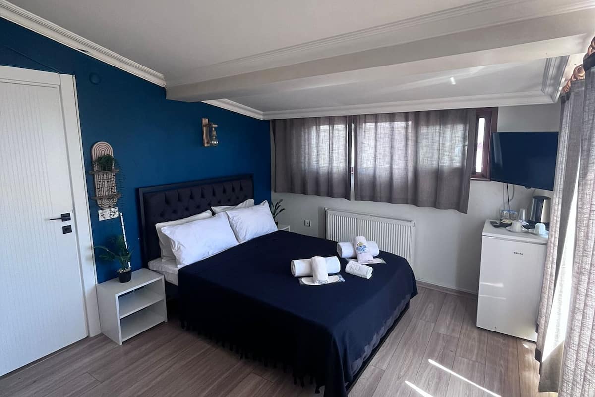 A bedroom with a bed, bedside tables, a radiator, a desk, and a window with curtains.