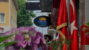 A hotel sign with a sun and water motif, a red flag with a white star, and a building with a yellow facade. - Blue Sea Hotel (Tuzla)