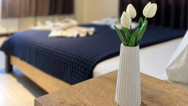 A bedroom with a bed, a white vase with flowers, and dark curtains. - Blue Sea Hotel (Tuzla)
