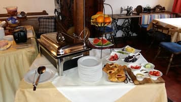 Ein reichhaltiges Buffet mit verschiedenen Speisen, darunter Obst, Gemüse und Gebäck, in einem Raum mit einer alten Nähmaschine und einem Holzstuhl.