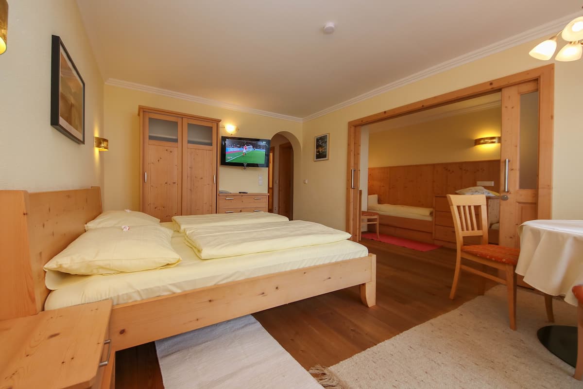 A bedroom with a wooden bed, a TV mounted on the wall, and a wooden wardrobe.