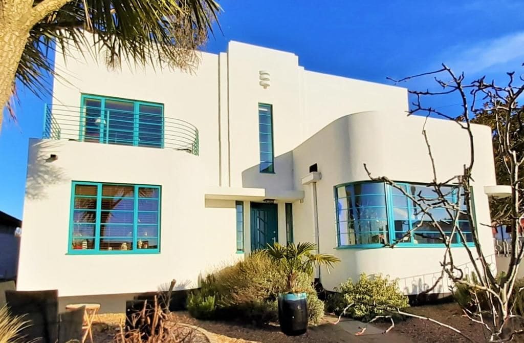 A modern two-story building with a white facade and green accents, including windows and doors.