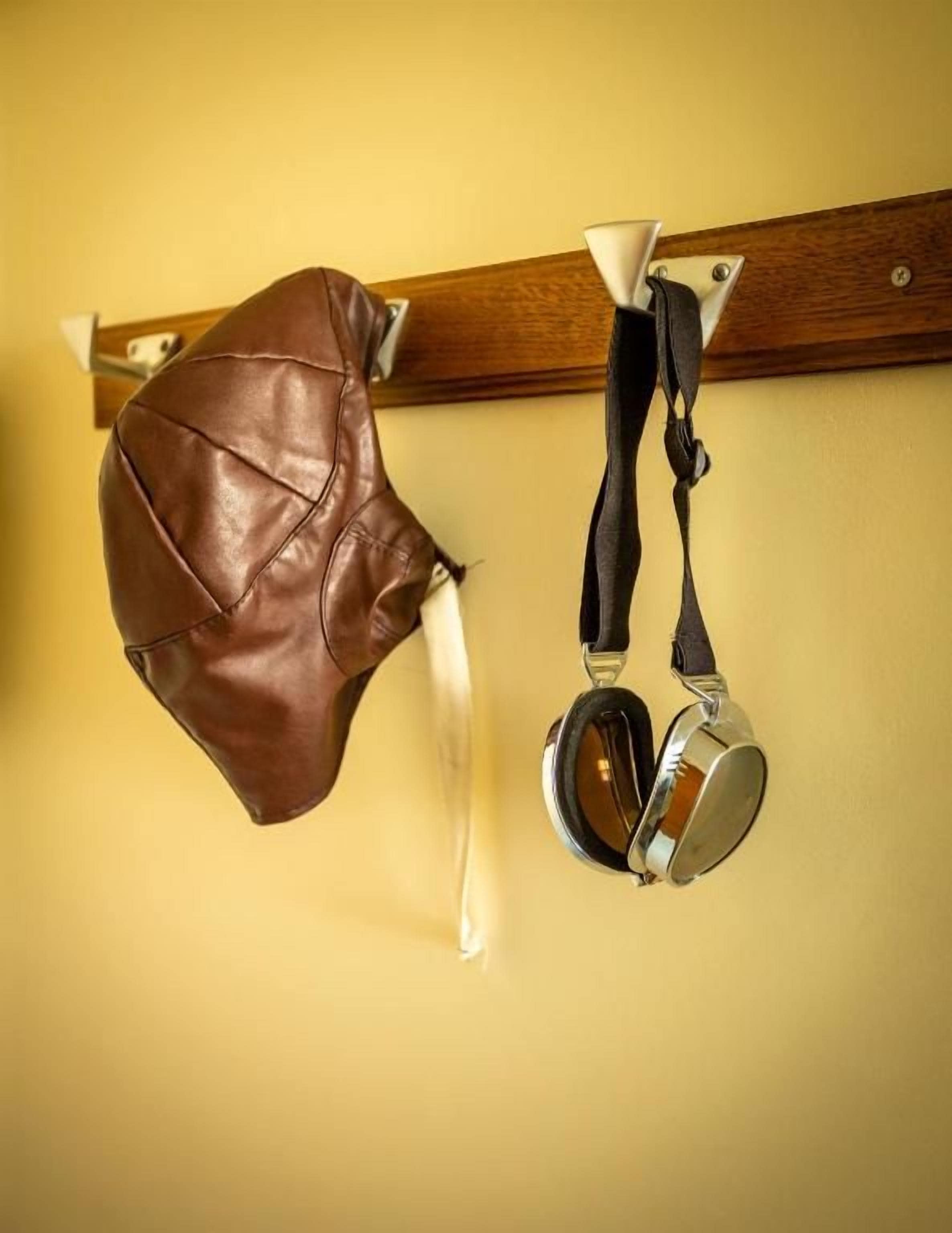 A brown leather bag and a black and silver object hanging on a wooden beam.