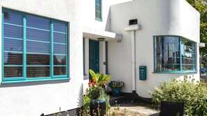 A modern white building with teal window frames and a small porch area with outdoor furniture. - Twentieth Century B&B (Birchington)