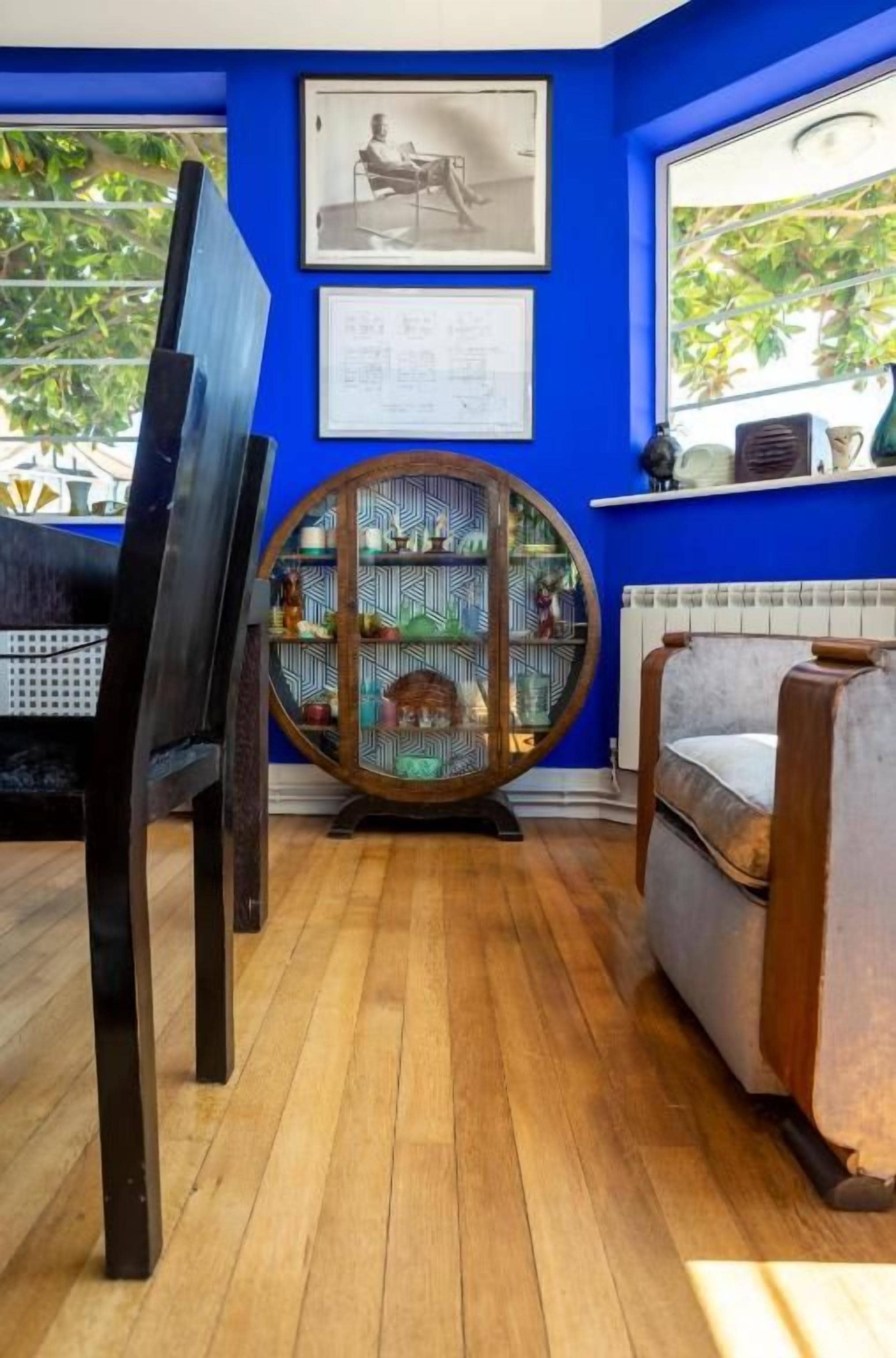Een kamer met een blauwe wand, een houten vloer, een rond houten kastje en een stoel.