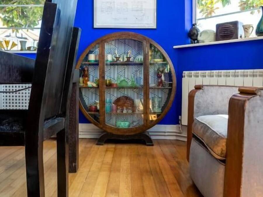 Een kamer met een blauwe wand, een houten vloer, een rond houten kastje en een stoel.