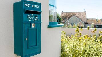 A teal-colored post office mailbox mounted on a white wall with a clear glass window nearby.