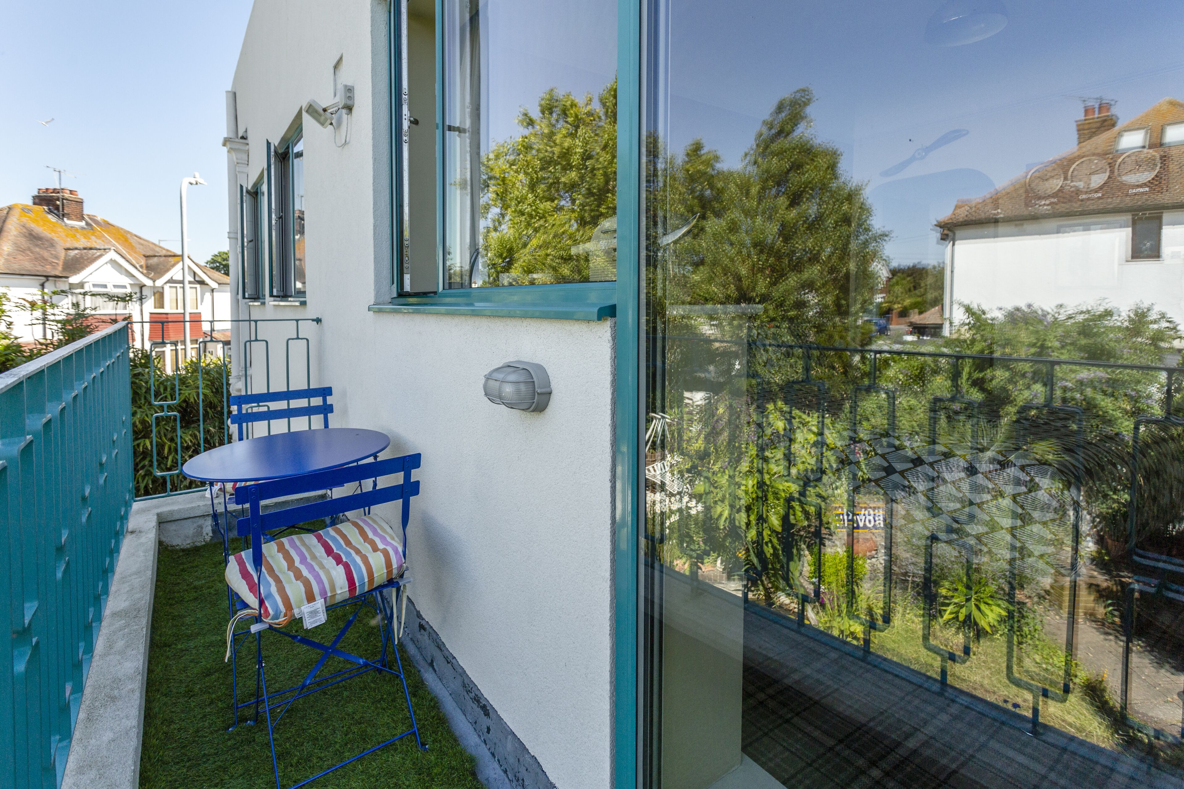 Un balcón con una pequeña mesa y silla, una ventana y vistas al vecindario.