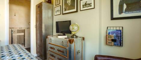 A bedroom with a bed, a dresser, a television, a globe, and framed pictures on the wall.
