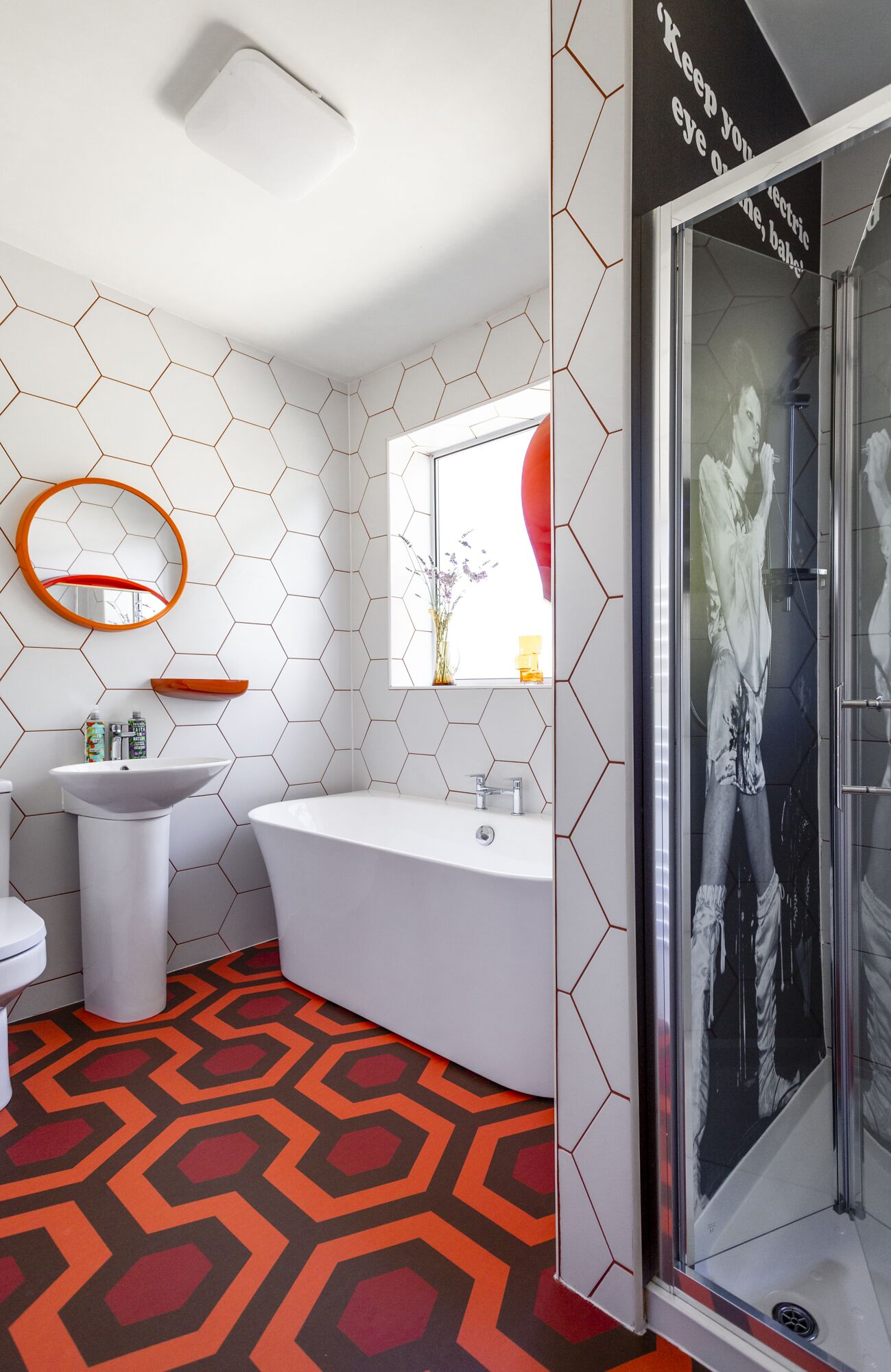 Um banheiro moderno com um padrão de azulejos hexagonais, uma banheira livre, uma pia branca e um box de vidro.