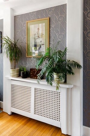 A white console table with a patterned wallpaper backdrop, a framed picture, and potted plants. - Twentieth Century B&B (Birchington)