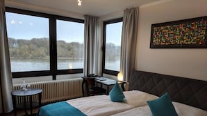 A hotel room with two beds, a view of a lake, a table with a chair, and a radiator. - Rheinterrassen Hotel Café Restaurant (Bornheim)