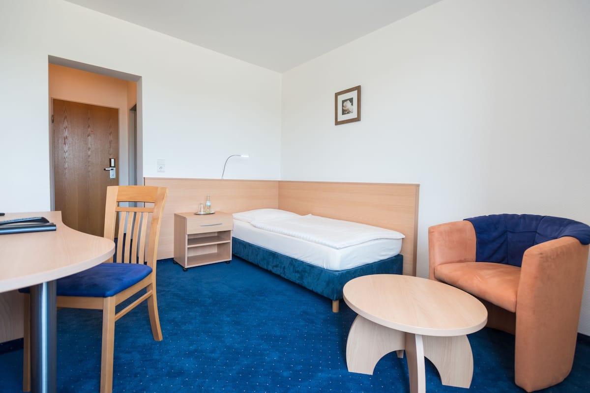 A compact hotel room with a single bed, a desk, a chair, and a small table.