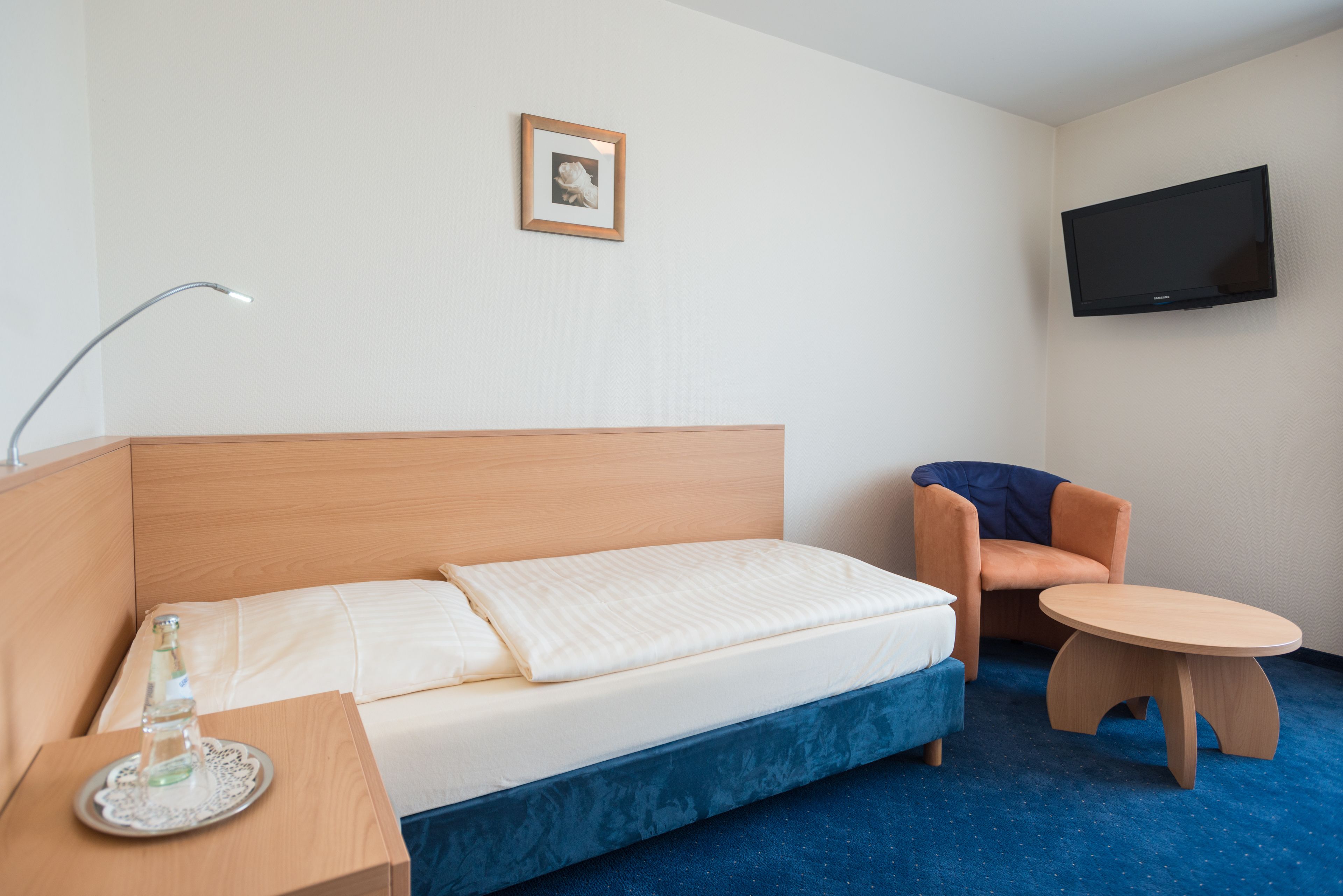 A hotel room with a bed, a chair, a small table, a TV, and a picture on the wall.