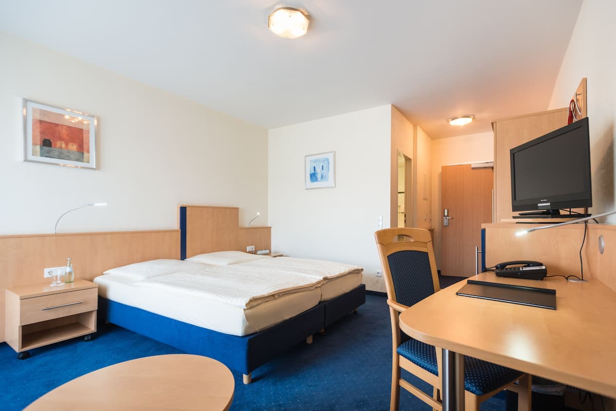 A hotel room with a bed, desk, chair, and television.