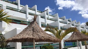 A building with white walls and green railings, featuring thatched umbrellas and potted plants. - Holiday Apartment, Beautiful one bedroom apartment, near to all amenities (Puerto del Carmen)