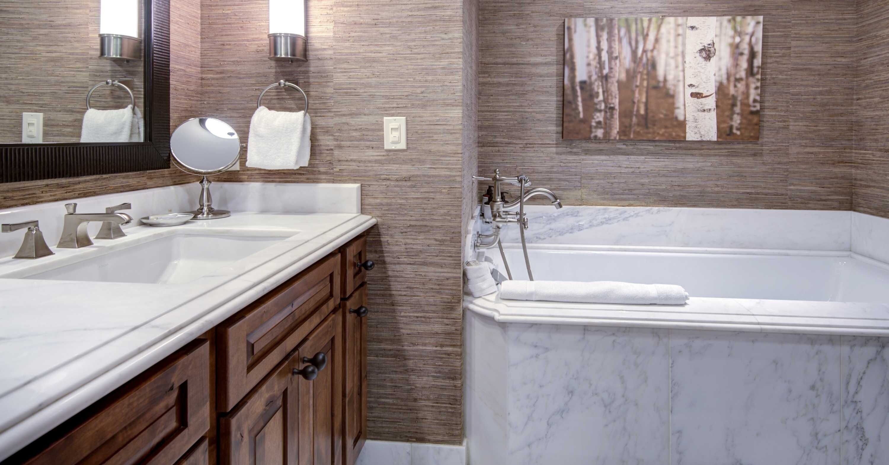 A bathroom with a marble sink, wooden vanity, a large mirror, a bathtub, and a wall-mounted towel rack.
