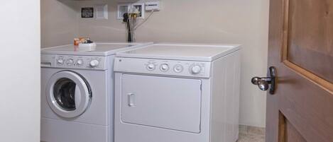 A laundry area with two white washing machines and a dryer, a wooden door, and a wall-mounted electrical outlet.