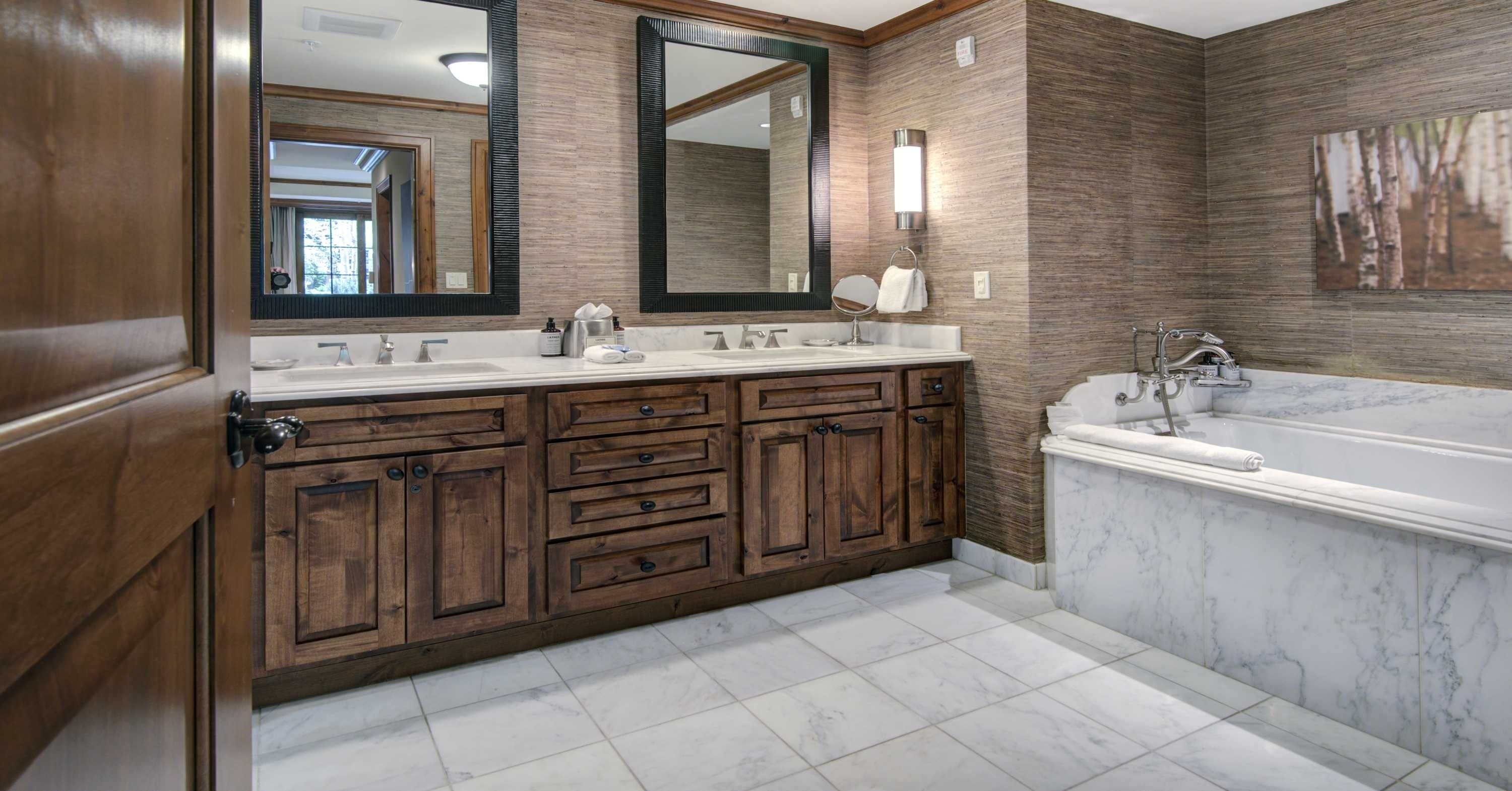 A bathroom with wooden cabinets, a double sink vanity, a large mirror, and a bathtub.