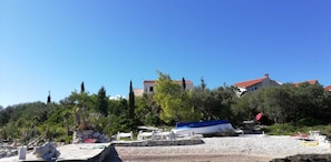 A beach with a boat, stone structures, and buildings in the background. - Apartments Grbin - Adults Only (Lumbarda)