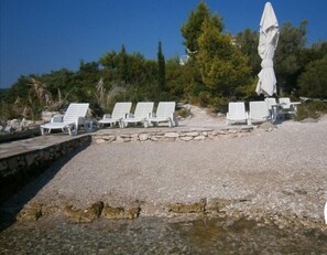 A beachside area with white lounge chairs and a stone wall. - Apartments Grbin - Adults Only (Lumbarda)