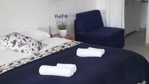 Quarto de hotel com duas camas, uma escrivaninha, uma cadeira, um abajur e um vaso com planta.