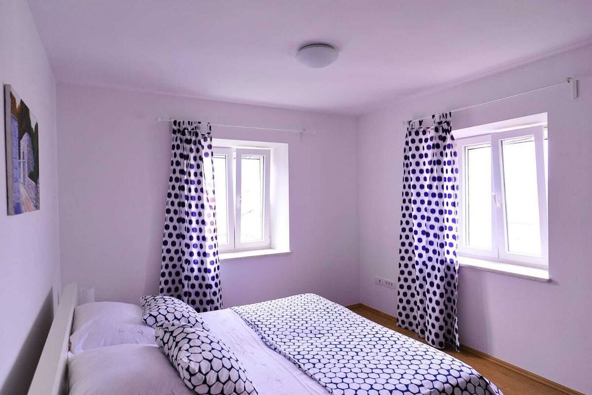 A bedroom with a bed, two windows, and polka dot curtains.