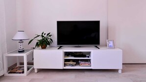 A white entertainment unit with a flat-screen TV, a lamp, and a potted plant. - Apartments An Ni - Adults Only (Korcula)