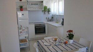A compact kitchen with white appliances, a dining table set for four, and a small window with curtains. - Apartments An Ni - Adults Only (Korcula)
