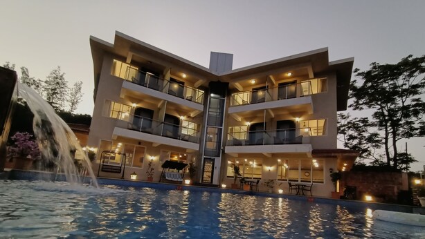 A multi-story hotel with a pool, outdoor seating, and a waterfall feature. - Bliss County Resort (Mahabaleshwar)