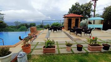 Zona junto a la piscina con vistas al mar, mobiliario exterior y plantas en macetas.