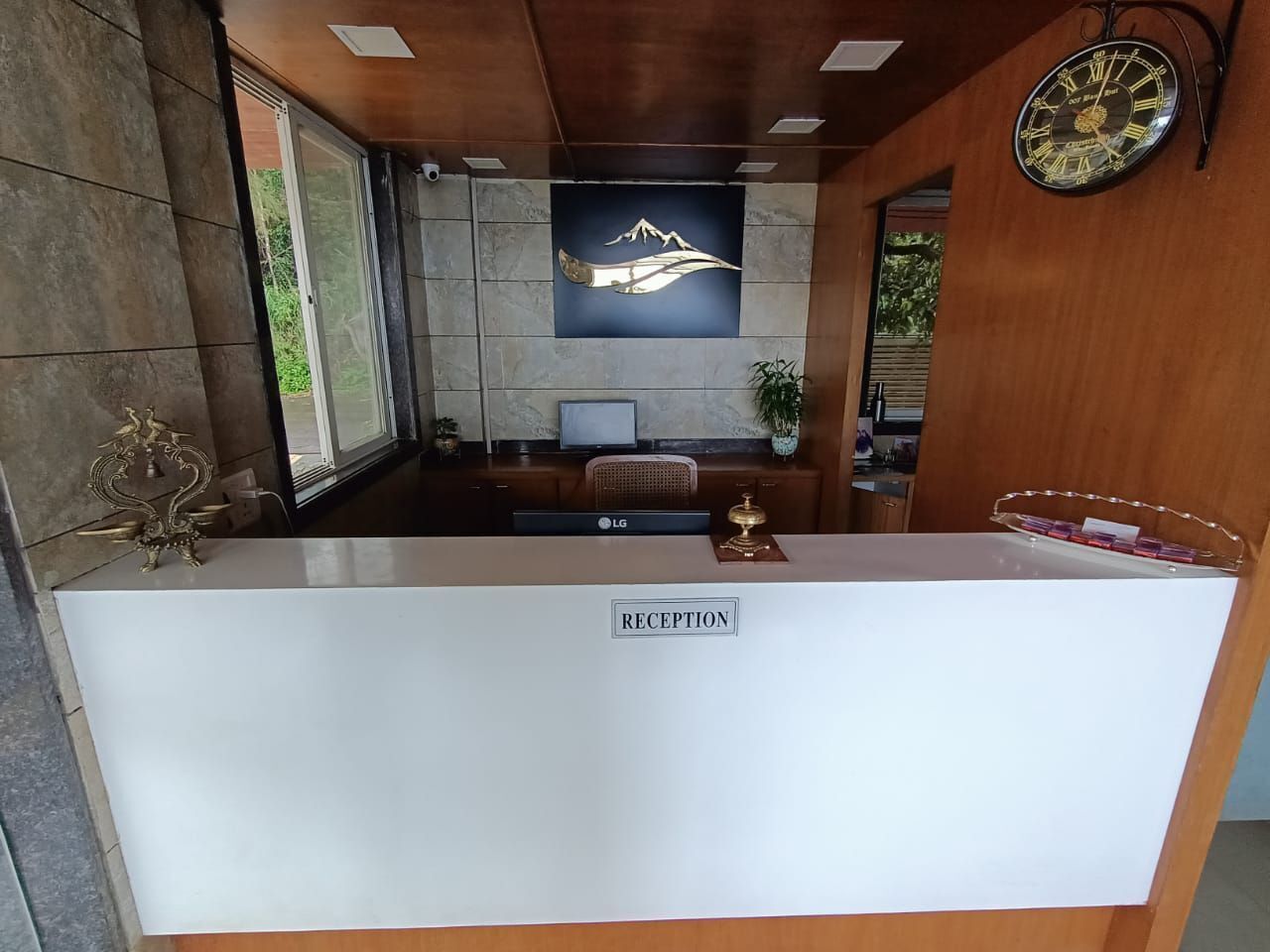 A reception desk with a "RECEPTION" sign, a clock, and a wall-mounted screen displaying a mountain and a hand.