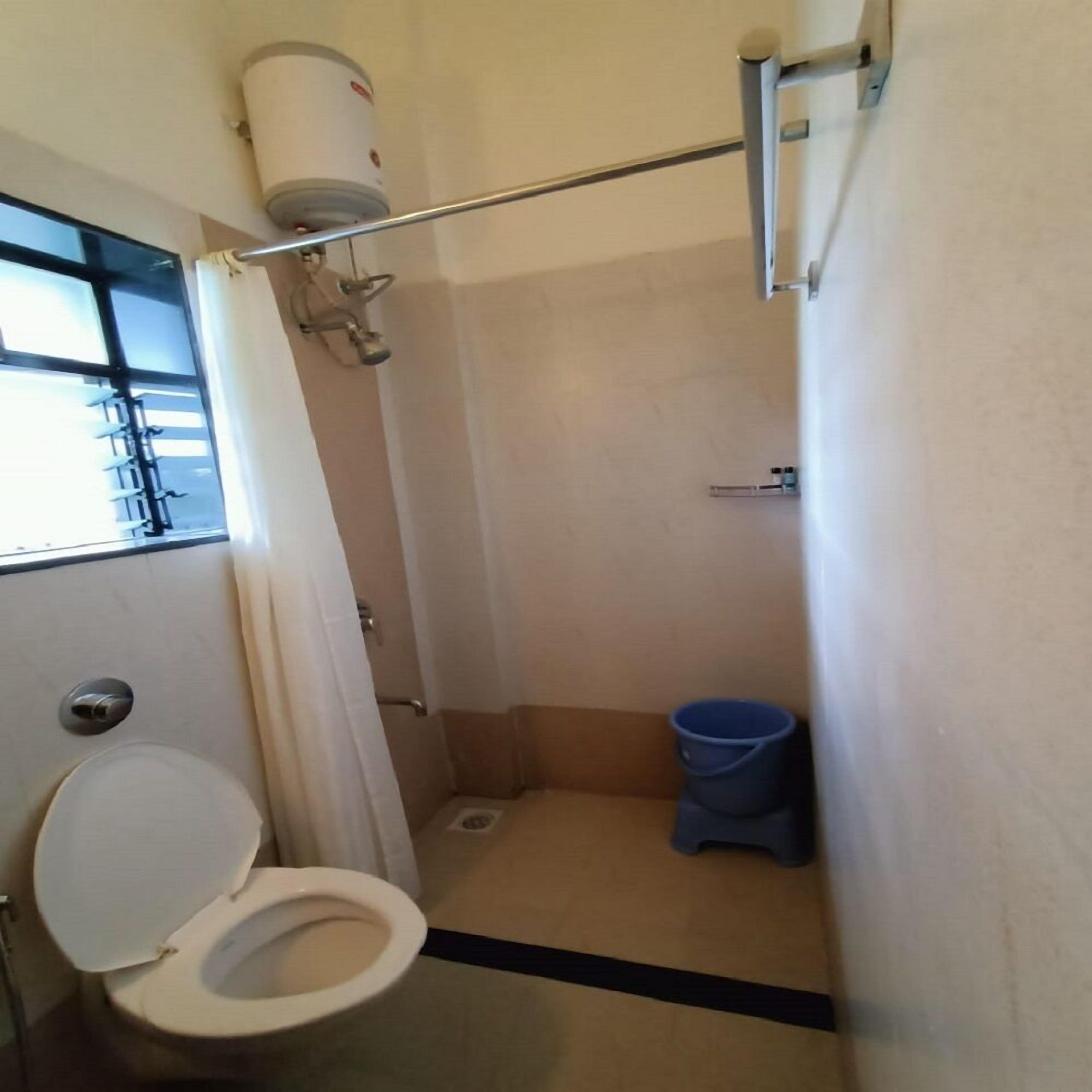 A small, narrow bathroom with a toilet, a shower, and a blue trash bin.