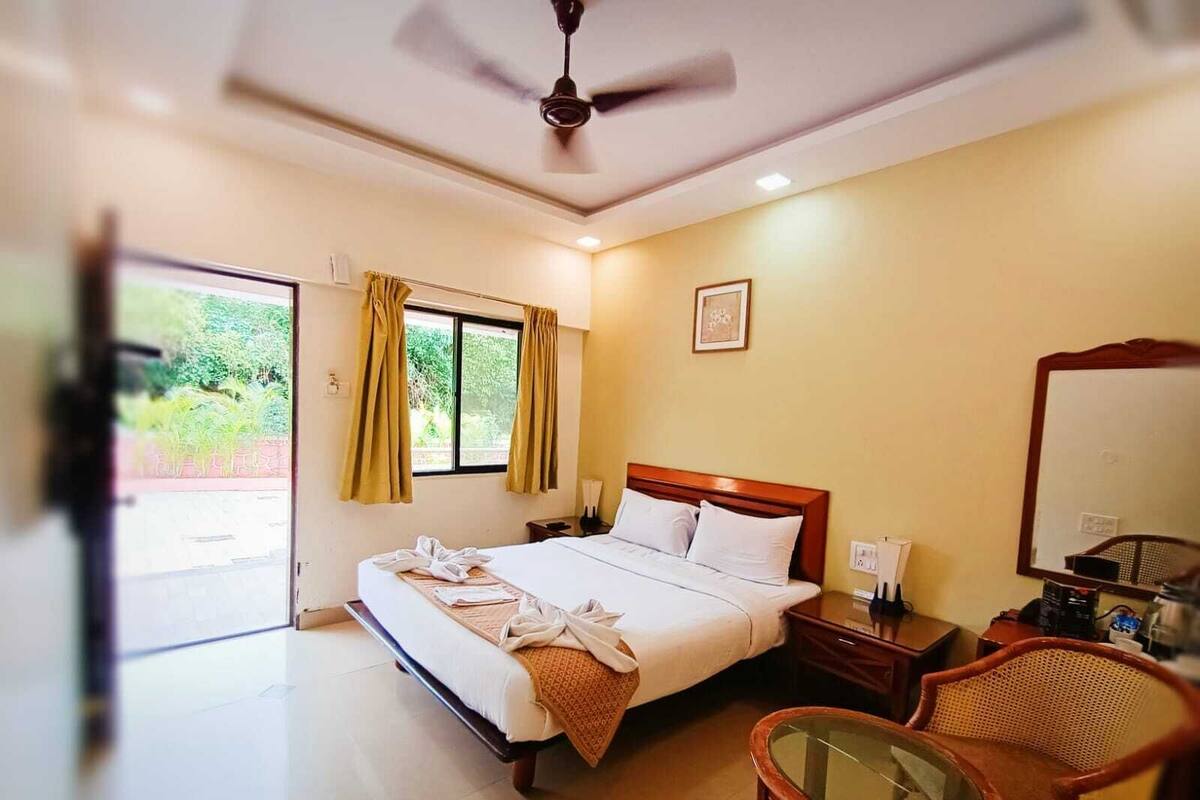 A hotel room with a bed, a chair, a table, a ceiling fan, and a window with curtains.
