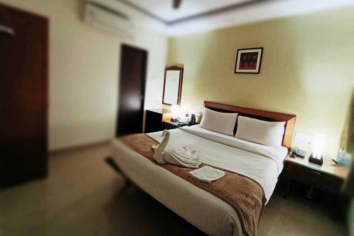 A hotel room with a bed, a bedside table, a nightstand, a ceiling fan, a framed picture on the wall, and a door.