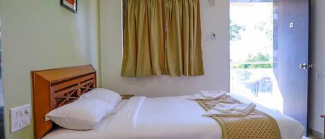 A bedroom with a bed, bedside table, and a view of the outdoors through a door.