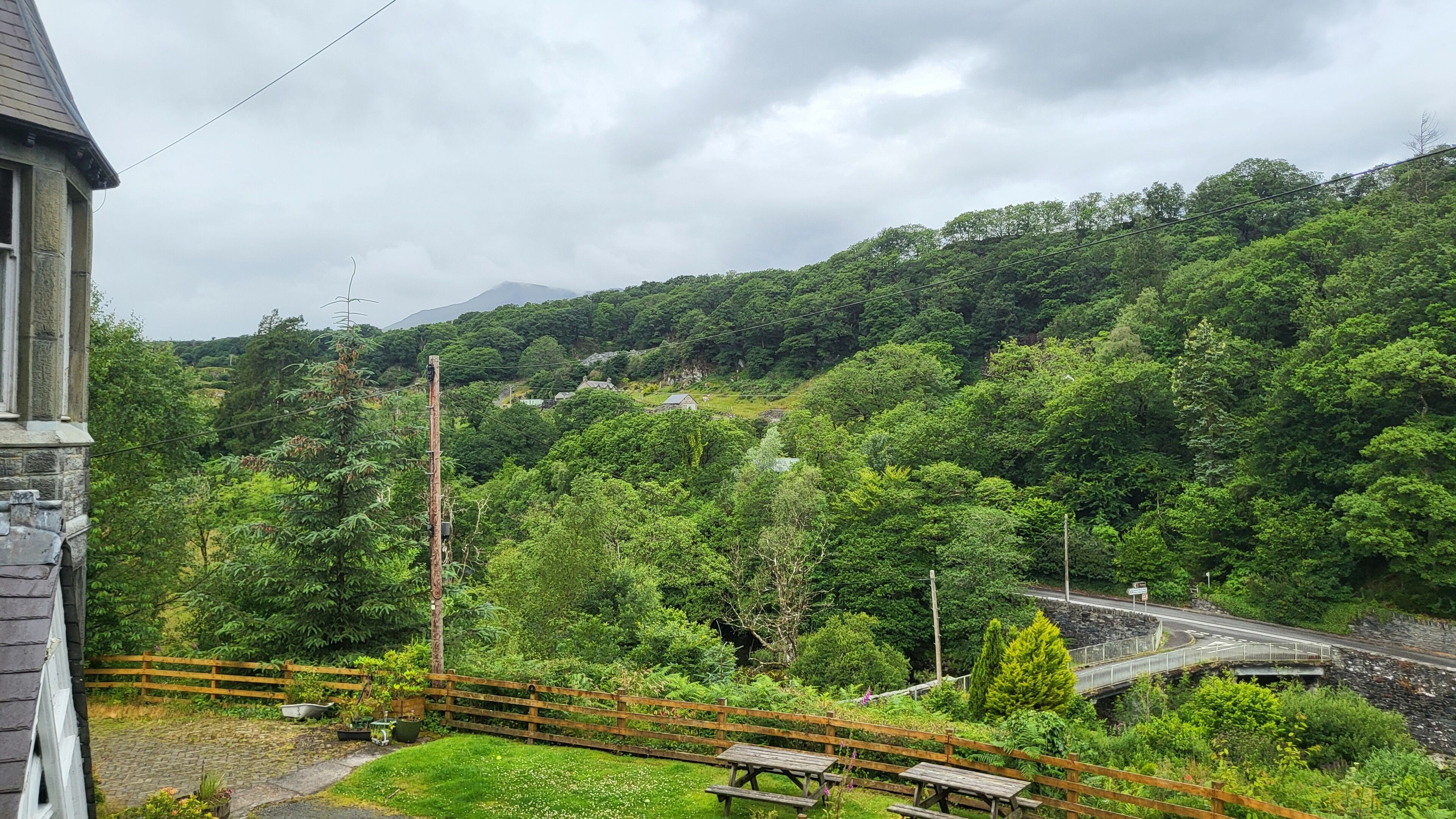 A lush green landscape with a stone building, a wooden fence, and a bridge over a stream.