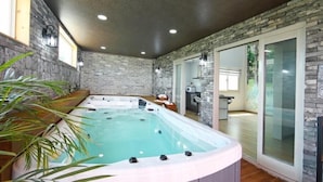 A spa area with a hot tub, a wooden bench, and a glass door leading to a kitchen.