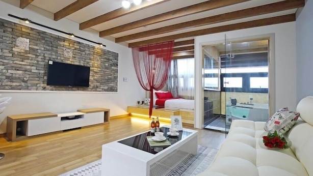 A modern living room with a stone wall, a flat-screen TV, a white sofa, and a glass door leading to a balcony.