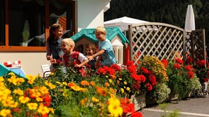 Un bâtiment à la façade blanche, une terrasse en bois avec une clôture à treillis et un petit jardin agrémenté de fleurs colorées.