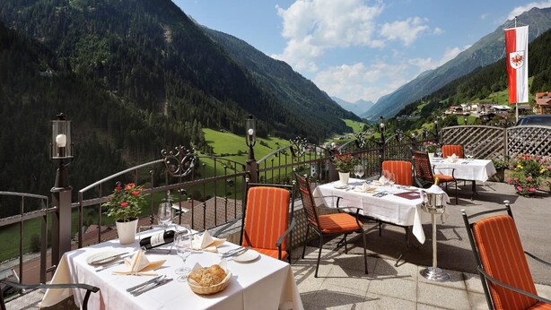 Un espace extérieur aménagé pour les repas, avec des tables pour deux personnes, offrant une vue sur un paysage montagneux.