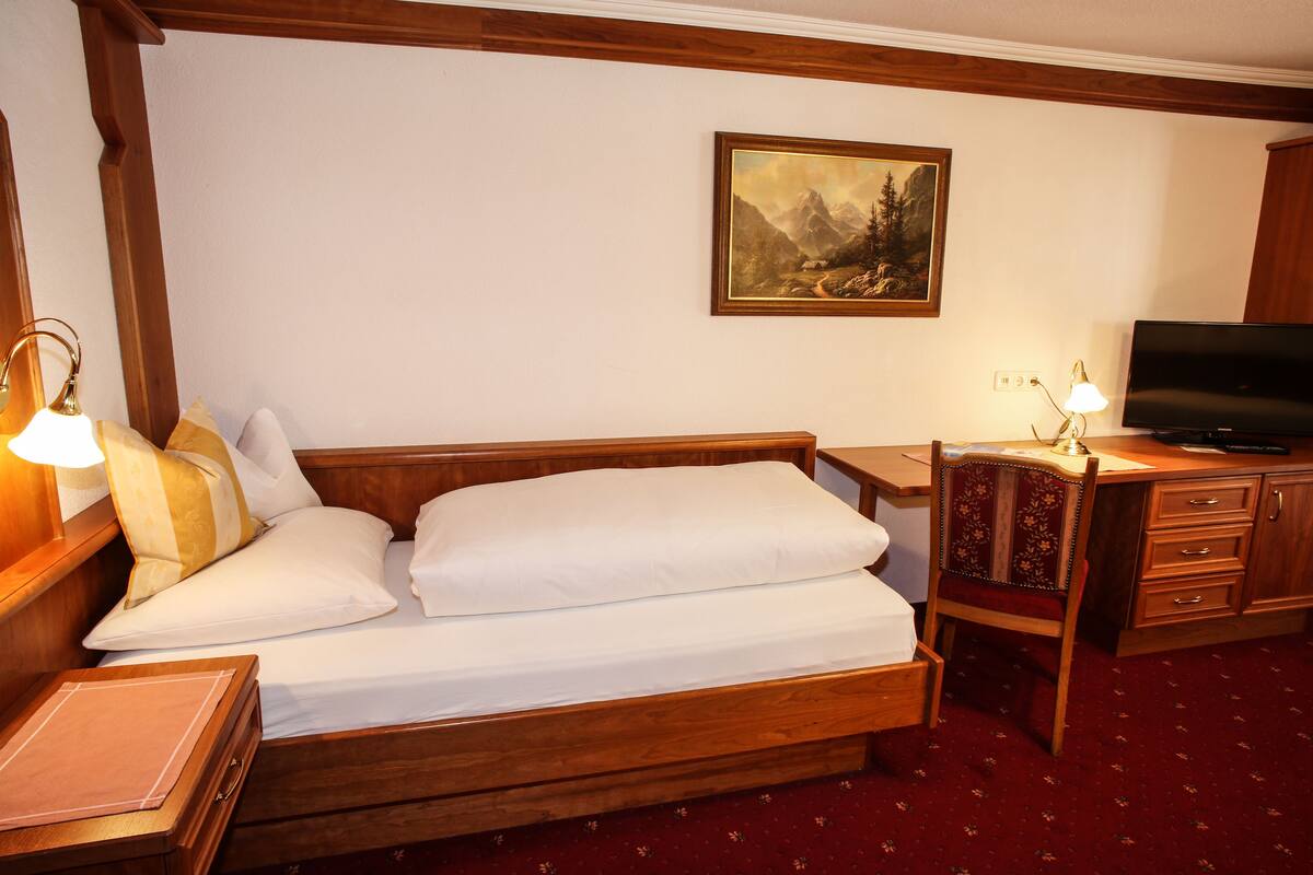Una habitación de hotel con una cama de madera, un escritorio con televisor y un cuadro en la pared.
