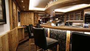 Un espace bar avec des lambris en bois, des fauteuils en cuir noir et un comptoir incurvé où sont exposés des verres.